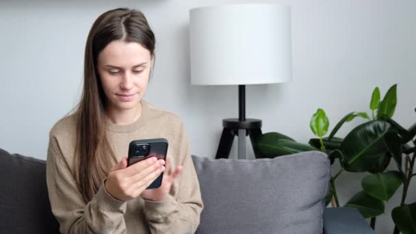Smiling Beautiful Young Female Sit Couch Looking Mobile Phone Screen — Vídeo de stock