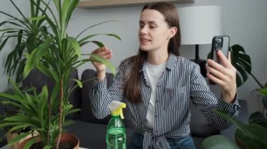 Gardener woman blogger enjoying pleasant conversation using mobile web camera video call application after transplants indoor plants. Concept plant care and home garden. Planting and social media
