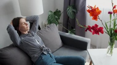 Side view of female fashion designer relaxing at workplace putting hands behind head. Calm happy young business woman chilling sitting on comfortable couch taking break at work in feminine studio