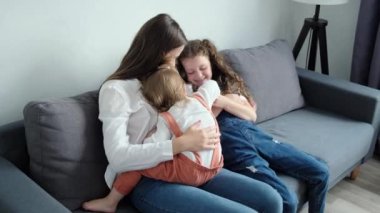 Playful happy young mom playing with two pretty little daughters, mother enjoy time on weekend with kids girls tickles laughing together seated on comfy sofa at home. Activities with child concept
