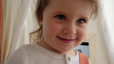 Selective focus of little girl child standing in cozy tent looking at camera waving hello greeting, webcam view baby preschool kid daughter doing hi goodbye gesture with hand, video conference concept