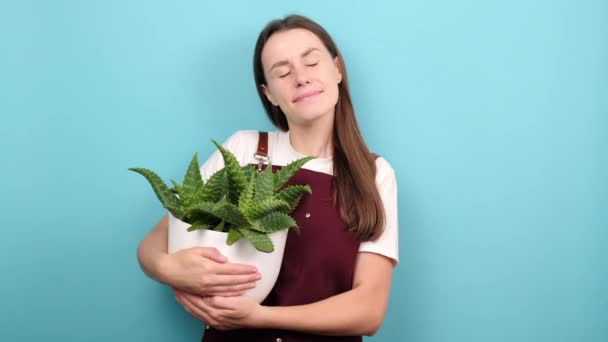 Pleased Young Woman Closes Eyes Embraces Pot Houseplant New Flower — Vídeo de Stock