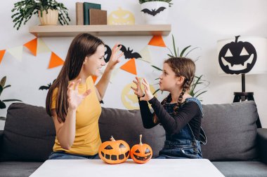 Oturma odasındaki rahat koltukta tatlı küçük kızıyla oturan neşeli genç anne ürkütücü Cadılar Bayramı hikayeleri anlatıyor. Komik anne ve kız çocuk evde eğleniyor. Kutlama ve sonbahar tatili konsepti