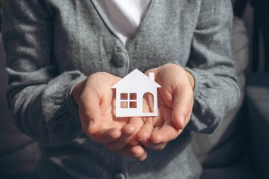 Uluslararası aileler günü, koruyucu aile bakımı, evde eğitim, sosyal mesafe. Beyaz kağıt ev modeli, aile evi, evsiz konutları ve sigorta konseptini elinde tutan kadın elleri