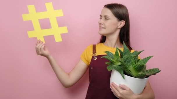 Porträtt Leende Unga Kvinnliga Innehav Kruka Växter Visar Gul Hashtag — Stockvideo