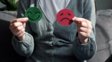 Kanepede oturan, elinde mutlu ve kızgın bir yüz kâğıdı tutan kadın ellerini kapat. Geri bildirim derecesi, duygusal zeka, denge duygu kontrolü, zihinsel sağlık değerlendirmesi, bipolar bozukluk konsepti