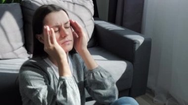 Sinir krizi, kriz konsepti. Kafasına dokunan yorgun esmer kız, baş ağrısı, migren, evdeki gri koltukta oturuyor. Bunalımlı genç bir kadın kayıp, keder ve travmayla baş ediyor.