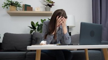 Dizüstü bilgisayara bakan endişeli genç bir kadın evdeki kanepede otururken hayal kırıklığına uğramış hissediyor. Stresli kadın kullanıcı, finansal sorunlar hakkında endişelenen bilgisayarı kullanıyor, günlüğe notlar yazıyor.