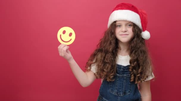 照片上 戴着圣诞礼帽的可爱的小女孩抱着小黄滑稽的脸 在工作室里通过红色的背景墙摆出一副孤身一人的样子 圣诞及新年2023假期概念 — 图库视频影像