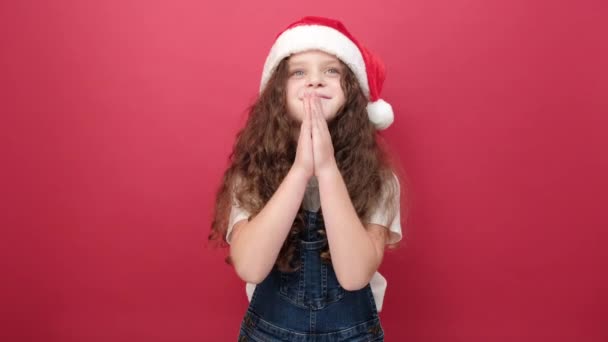 快乐可爱的小女孩戴着圣诞礼帽交叉着手指 相信好运会让愿望在工作室的红颜色的背景墙上出现 人与寒假概念 — 图库视频影像