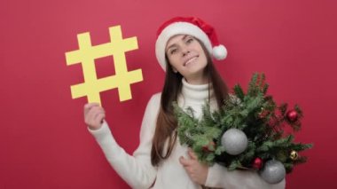 Noel Baba şapkalı gülümseyen genç kadının portresi kırmızı arka planda izole edilmiş, sosyal ağda viral konunun yaygınlaştırıldığı hashtag sembolü içeriyor. Mutlu yıllar konsepti