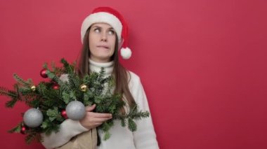 Gülümseyen genç Noel Baba kadın 20 'li yaşlarda elinde ladin dalları buketi ve sarı boş bulut, kırmızı arka planda izole edilmiş konuşma balonu var. Yeni yılı kutluyoruz. Mutlu tatiller.