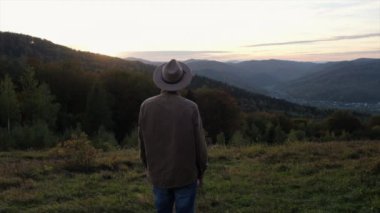 Şapka atan ve kameraya bakan neşeli genç adam, arka planda duran sakallı gezgin adam muhteşem günbatımında ya da gün doğumunda güzel sonbahar dağlarında. Seyahat ve seyahat tutkusu konsepti