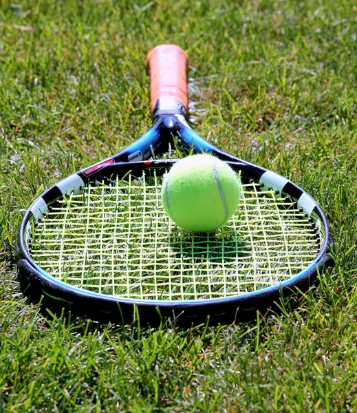 Tennis racket with ball on grass court — Stock Photo, Image