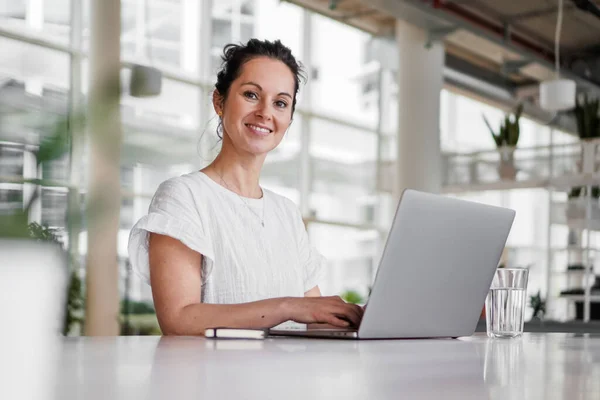 happy smiling  successful remote working dark haired woman cheerful infront of laptop or notebook in casual outfit sitting on work desk in her modern loft living room home office having a video chat