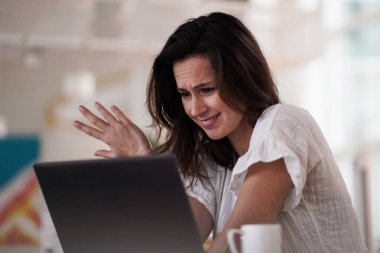 Bunalımlı, uzaktan kumandalı, kahverengi saçlı bir kadın bilgisayarın başında hayal kırıklığına uğramış bir şekilde oturuyor. Ya da çalışma masasının üzerindeki çalışma masasında, parlak, modern oturma odasındaki çalışma odasında. 