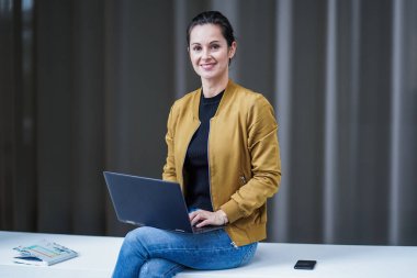 Modern bir otel lobisinde dizüstü bilgisayarıyla ya da defteriyle bacak bacak bacak üstüne atmış, mutlu, uzaktan kumandalı, mutlu bir çalışan kadın. 