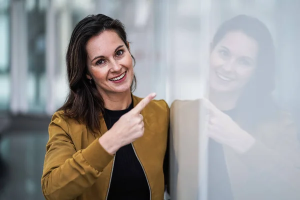 幸せな笑顔カジュアルなビジネス女性指して指でカメラであなたに直接対処するためにモチベーションに囲まれて現代的な白い屋内の壁 — ストック写真