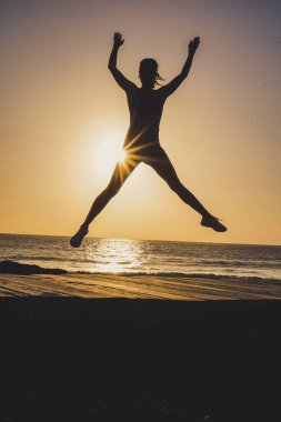 Gün batımında ya da gün doğumunda sahilde başarılı bir atlama ve neşeli bir kadının silüeti motivasyon için.