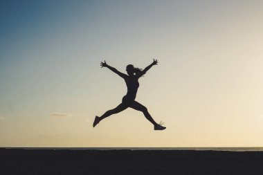 Gün batımında ya da gün doğumunda sahilde başarılı bir atlama ve neşeli bir kadının silüeti motivasyon için.