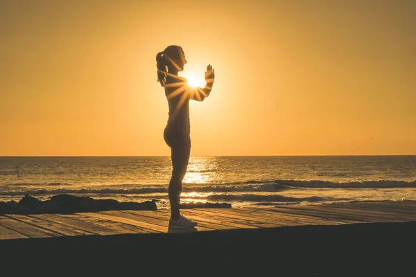 ビーチボードウォークでヨガ 瞑想を練習するナマステポーズのスポーツ女性のシルエット日没や日の出の間に — ストック写真