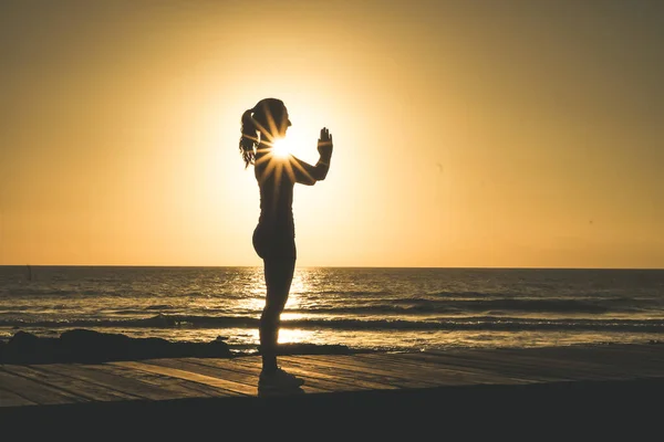 ビーチボードウォークでヨガ 瞑想を練習するナマステポーズのスポーツ女性のシルエット日没や日の出の間に — ストック写真