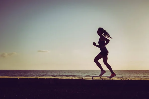 Silhueta Uma Mulher Atlética Correndo Esportiva Calçadão Praia Durante Pôr — Fotografia de Stock