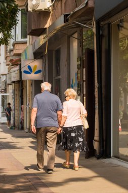 Sofya, Bulgaristan - 13.07.2019. Şehrin sakinlerinin hayatları. Yürüyüşe çıkmış yaşlı bir çift. Büyükbabam ve büyükannem el ele şehrin caddesinde yürürler..