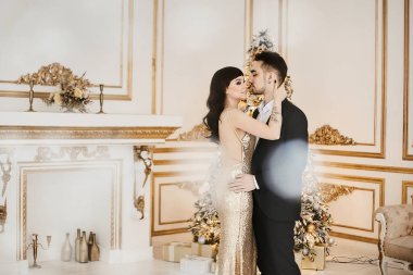 Altın elbiseli genç bir kadın ve Noel için dekore edilmiş takım elbiseli yakışıklı bir adam.