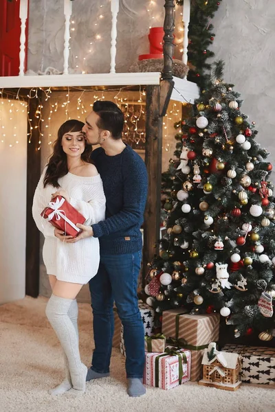 英俊的年轻人在一棵装饰过的圣诞树旁边送给他可爱的女朋友一份圣诞礼物 — 图库照片