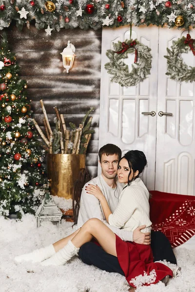 一对年轻夫妇在冬季乡村的室内摆姿势，用人造雪和圣诞树装饰新年 — 图库照片
