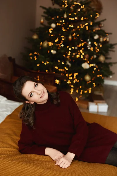 Parlak makyajlı, kırmızı örgü elbiseli, arka planda neşeli ışıklar olan yetişkin bir kadın model.