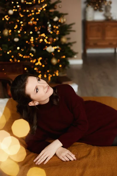 Parlak makyajlı, kırmızı örgü elbiseli, arka planda neşeli ışıklar olan yetişkin bir kadın.