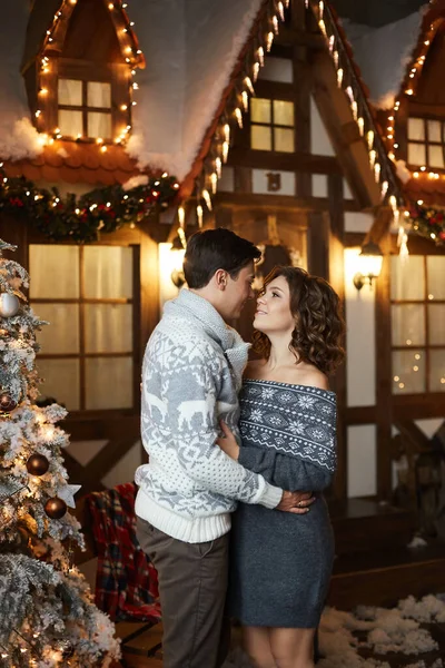 Jeune homme beau dans un pull confortable et jolie femme en robe confortable tricotée se regardant à côté d'un arbre de Noël — Photo