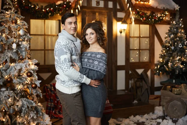 Doux couple à la mode dans des vêtements confortables posant à côté d'un arbre de Noël près de leur maison de campagne dans la soirée — Photo