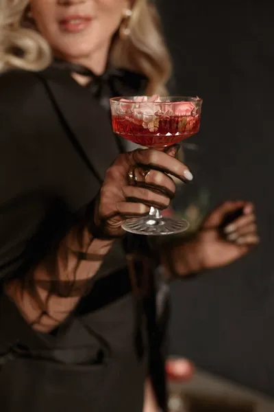 A luxurious glass of red alcohol cocktail with ice in the hand of a gorgeous young blonde woman — Stock Photo, Image