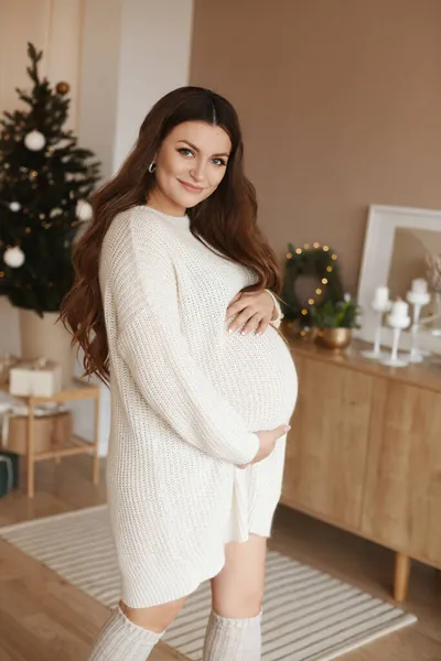 Schöne schwangere Model Mädchen hält ihren Bauch und schaut in die Kamera, während posiert in geschmückten für Weihnachten Interieur — Stockfoto