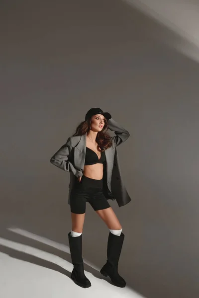 Bedårande modell kvinna i svart bh, fashionabla kavaj och trendiga stövlar på den grå bakgrunden — Stockfoto
