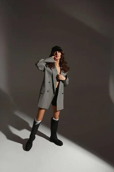 Söt modell flicka i en fashionabel överdimensionerad kavaj, behå och fashionabla stövlar över grå bakgrund — Stockfoto