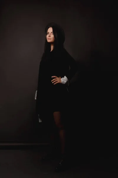 Charmig modell flicka i svart trendig hatt och kort svart klänning poserar på svart bakgrund — Stockfoto