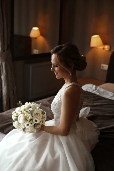 Retrato de una novia encantadora feliz en vestido de novia elegante posando con un ramo de novia en el interior — Foto de Stock