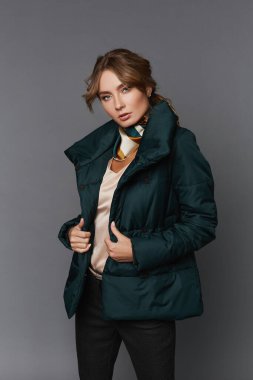 Gri arka planda zarif, kalın ceketli, sarı saçlı, çekici bir manken kız.