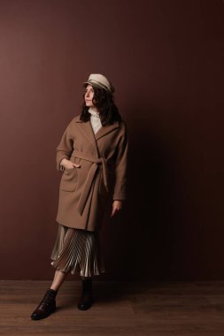 Hoş, orta yaşlı, modaya uygun giyinmiş bir kadın model. Çekici yetişkin bir kadın moda bir ceket, bere, etek, içeride poz veriyor.