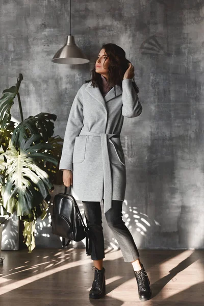 Inomhus fullängds porträtt av en elegant kvinna klädd i en grå trendig rock, trendiga skor, poserar med en klassisk svart ryggsäck. Höst och vår mode reklam koncept — Stockfoto