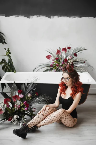 穿着黑色紧身衣和时髦靴子在浴室里摆姿势的红头发年轻女人很迷人 — 图库照片