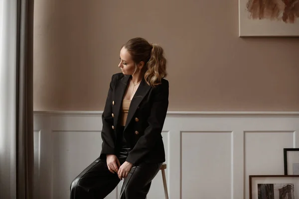 Vágott portré egy divatos fiatal nő divatos smink visel stílusos blézer és fekete nadrág pózol a nappaliban — Stock Fotó