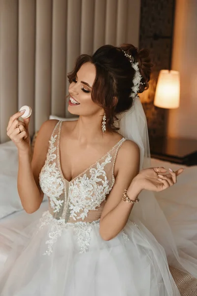 Splendida giovane donna in un abito da sposa godendo gustoso dessert mentre seduto sul letto — Foto Stock