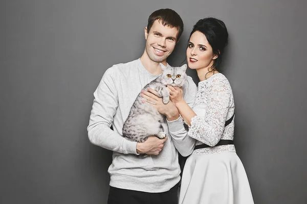 Feliz casal querida com gato bonito posando sobre fundo cinza. Dia dos Namorados conceito publicidade — Fotografia de Stock