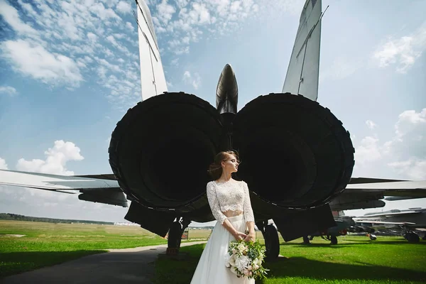 A young beautiful brown-haired bride is standing behind a jet plane — Stockfoto
