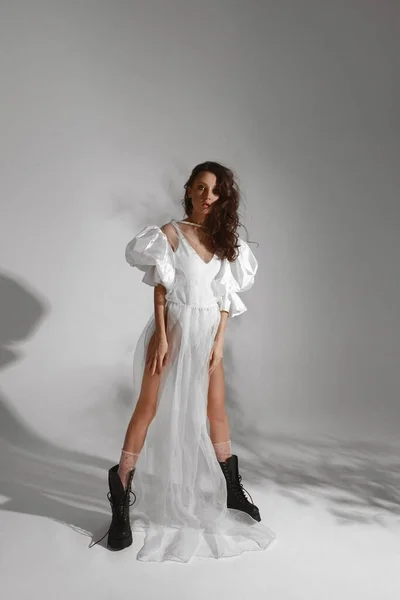 Νεαρή γοητευτική γυναίκα σε λευκό φόρεμα με διάφανη φούστα και μαύρα μοντέρνα ψηλά παπούτσια στο γκρι φόντο. Άνοιξη και καλοκαίρι τάσεις της μόδας — Φωτογραφία Αρχείου
